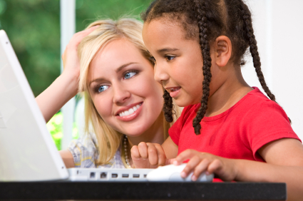 A beautiful young mother and her mixed race young daughter using a latop at home in the kitchen.